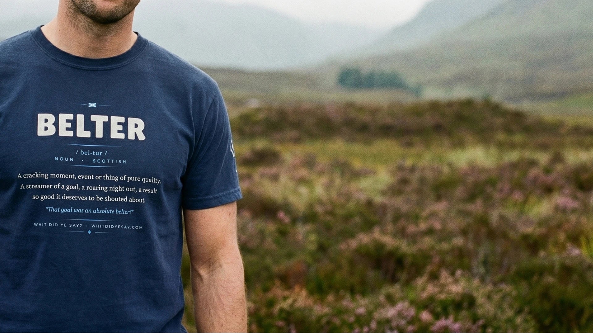 A man wearing the navy BELTER dictionary definition tee in the Scottish hills